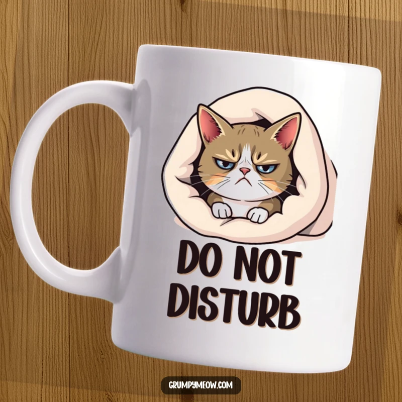 Funny grumpy cat mug, peeking with a frown from beneath a cozy blanket, embodying morning reluctance.