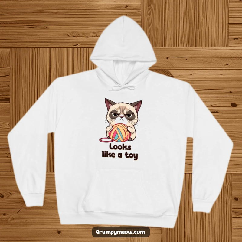 Funny grumpy cat with narrowed eyes, judging a brightly colored ball of yarn on a hoodie, for cozy scrutiny, an ideal funny gift.